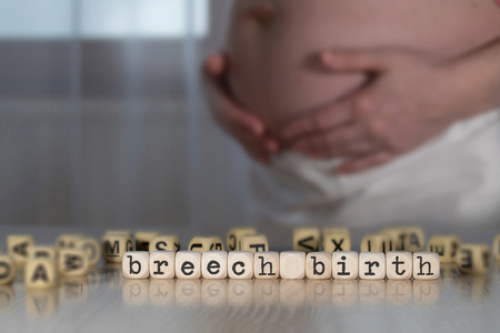 Words BREECH BIRTH composed of wooden letters. Pregnant woman in the backgroundの写真素材