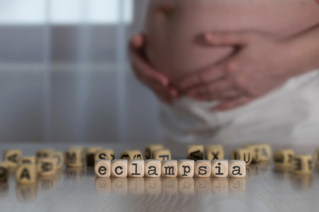 Word ECLAMPSIA  composed of wooden letters. Pregnant woman in the backgroundの写真素材