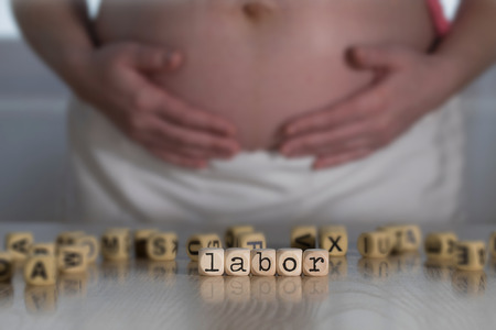 Word LABOR composed of wooden letters. Pregnant woman in the backgroundの写真素材
