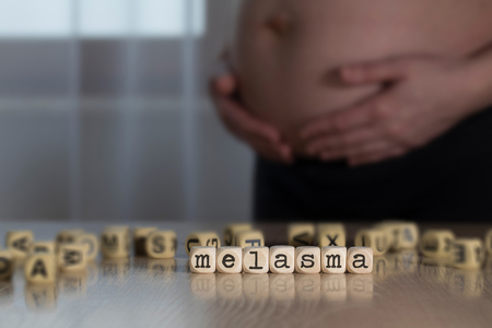 Word MELASMA composed of wooden letters. Pregnant woman in the backgroundの写真素材