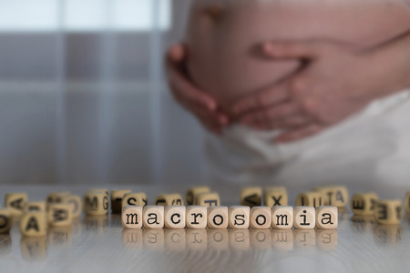 Word MACROSOMIA  composed of wooden letters. Pregnant woman in the backgroundの写真素材