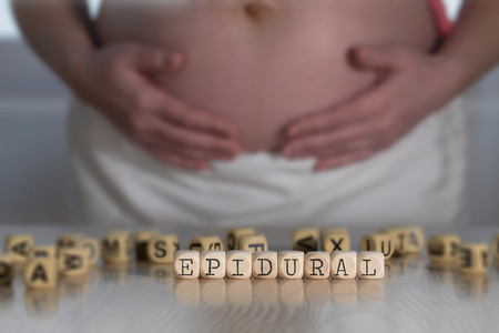 Word EPIDURAL composed of wooden letters. Pregnant woman in the backgroundの写真素材