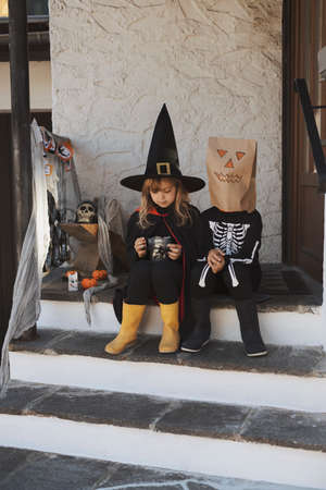 Kids in Halloween costumes are sitting on the porchの写真素材