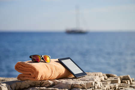 black e-reader, orange towel and sunglasses laying on a rock near to Istrian seaの写真素材