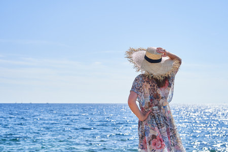 A woman is seen from behind. clothes fluttering in the wind. straw hat.の写真素材