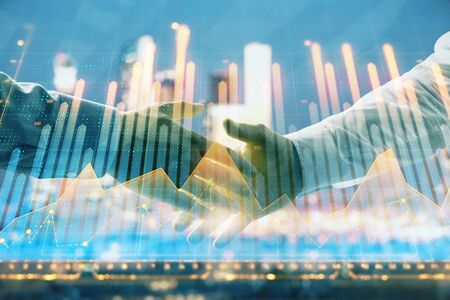 Double exposure of financial chart on cityscape background with two businessmen handshake. Concept of financial analysis and investment opportunitiesの写真素材