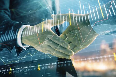 Double exposure of financial chart on cityscape background with two businessmen handshake. Concept...