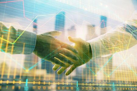 Double exposure of financial graph on cityscape background with two businessman handshake. Concept of stock market dealの写真素材