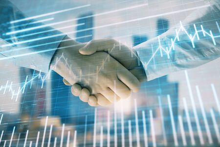 Double exposure of financial graph on cityscape background with two businessman handshake. Concept of stock market dealの写真素材