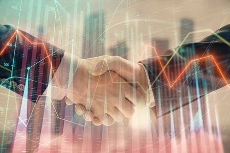 Double exposure of financial graph on cityscape background with two businessman handshake. Concept of stock market dealの写真素材