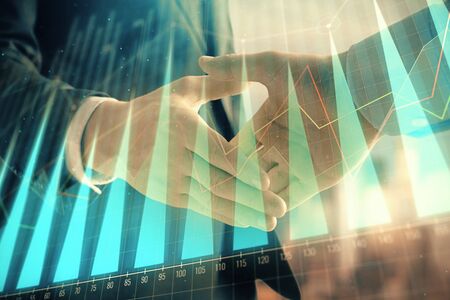 Double exposure of financial graph on cityscape background with two businessman handshake. Concept of stock market dealの写真素材