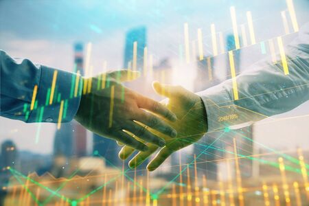 Double exposure of financial graph on cityscape background with two businessman handshake. Concept...