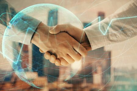 Double exposure of financial chart and world map on cityscape background with two businessmen handshake. Concept of international investmentの写真素材