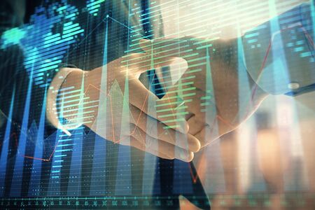 Double exposure of financial chart and world map on cityscape background with two businessmen handshake. Concept of international investmentの写真素材