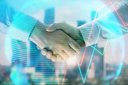 Double exposure of financial chart and world map on cityscape background with two businessmen handshake. Concept of international investmentの写真素材