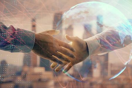 Double exposure of world map on cityscape background with two businessmen handshake. Concept of international businessの写真素材