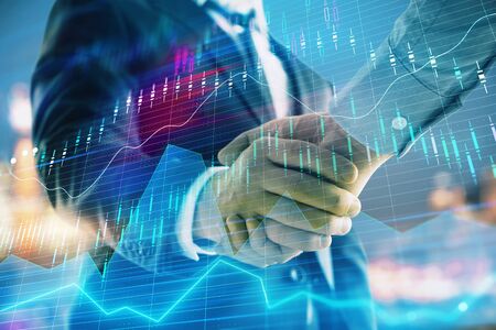 Double exposure of financial chart on cityscape background with two businessmen handshake. Concept of financial analysis and investment opportunitiesの写真素材