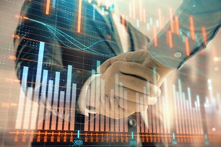 Double exposure of financial graph on cityscape background with two businessman handshake. Concept of stock market dealの写真素材