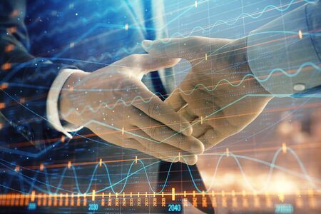Double exposure of financial chart on cityscape background with two businessmen handshake. Concept of financial analysis and investment opportunitiesの写真素材