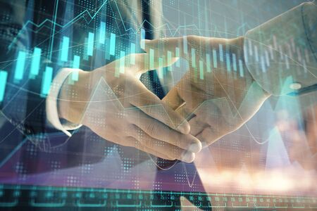 Double exposure of financial chart on cityscape background with two businessmen handshake. Concept of financial analysis and investment opportunitiesの写真素材
