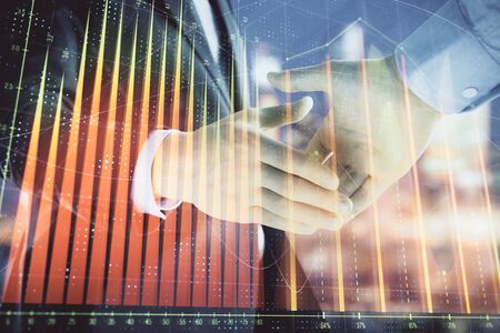 Double exposure of financial chart on cityscape background with two businessmen handshake. Concept of financial analysis and investment opportunitiesの写真素材