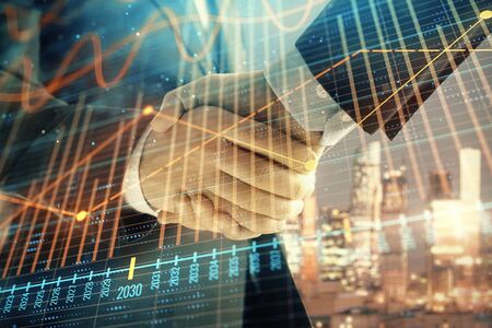 Double exposure of financial chart on cityscape background with two businessmen handshake. Concept of financial analysis and investment opportunitiesの写真素材