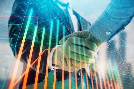 Double exposure of financial graph on cityscape background with two businessman handshake. Concept of stock market dealの写真素材
