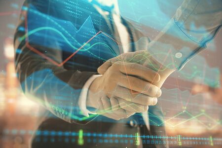 Double exposure of financial chart on cityscape background with two businessmen handshake. Concept of financial analysis and investment opportunitiesの写真素材