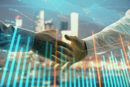 Double exposure of financial chart on cityscape background with two businessmen handshake. Concept of financial analysis and investment opportunitiesの写真素材