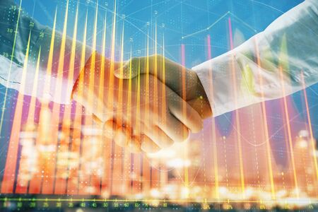 Double exposure of financial chart on cityscape background with two businessmen handshake. Concept of financial analysis and investment opportunitiesの写真素材