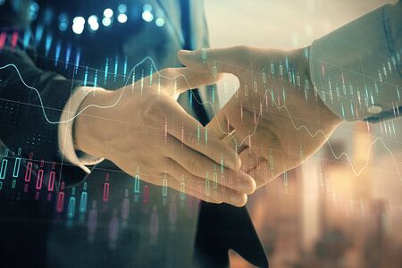 Double exposure of financial graph on cityscape background with two businessman handshake. Concept of stock market dealの写真素材