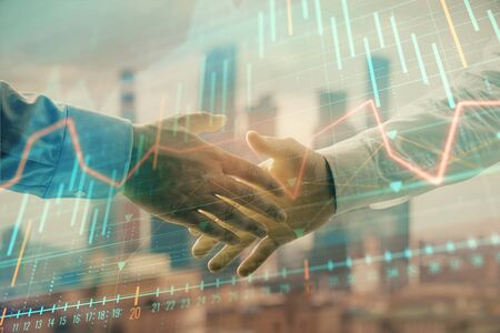 Double exposure of financial graph on cityscape background with two businessman handshake. Concept of stock market dealの写真素材