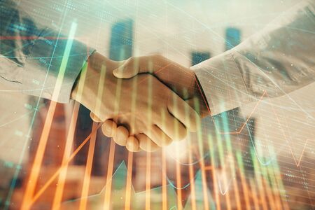Double exposure of financial graph on cityscape background with two businessman handshake. Concept of stock market dealの写真素材