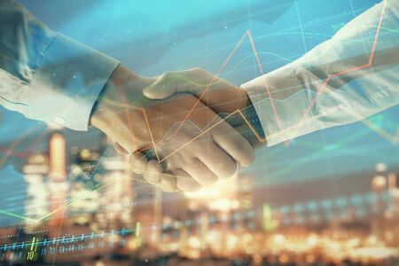 Double exposure of financial chart on cityscape background with two businessmen handshake. Concept of financial analysis and investment opportunitiesの写真素材