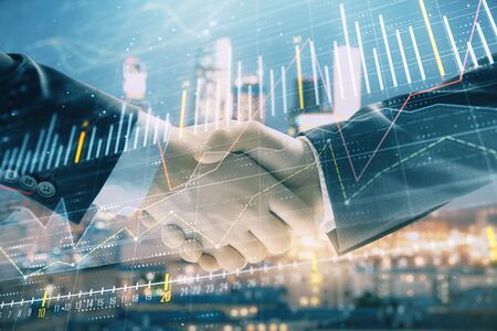Double exposure of financial chart on cityscape background with two businessmen handshake. Concept of financial analysis and investment opportunitiesの写真素材