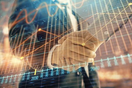 Double exposure of financial chart on cityscape background with two businessmen handshake. Concept of financial analysis and investment opportunitiesの写真素材