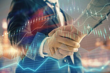 Double exposure of financial chart on cityscape background with two businessmen handshake. Concept of financial analysis and investment opportunitiesの写真素材