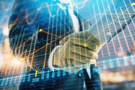 Double exposure of financial chart on cityscape background with two businessmen handshake. Concept of financial analysis and investment opportunitiesの写真素材