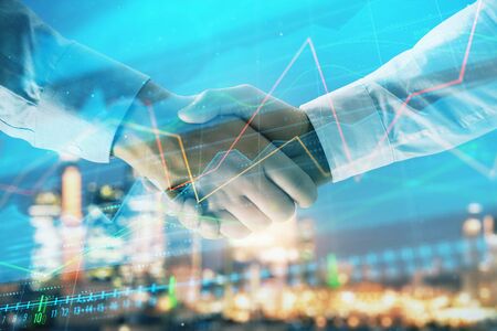 Double exposure of financial chart on cityscape background with two businessmen handshake. Concept of financial analysis and investment opportunitiesの写真素材