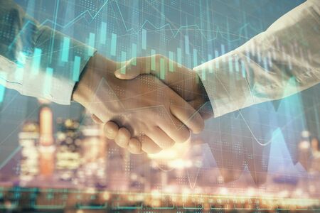 Double exposure of financial chart on cityscape background with two businessmen handshake. Concept of financial analysis and investment opportunitiesの写真素材