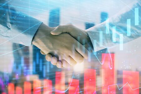 Double exposure of financial graph on cityscape background with two businessman handshake. Concept of stock market dealの写真素材