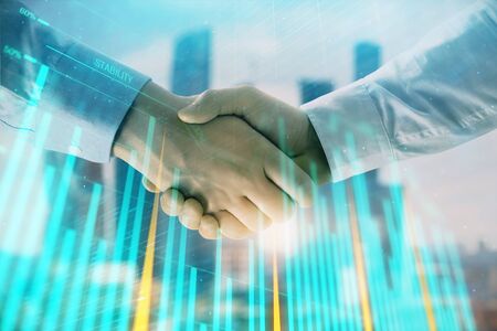 Double exposure of financial graph on cityscape background with two businessman handshake. Concept of stock market dealの写真素材