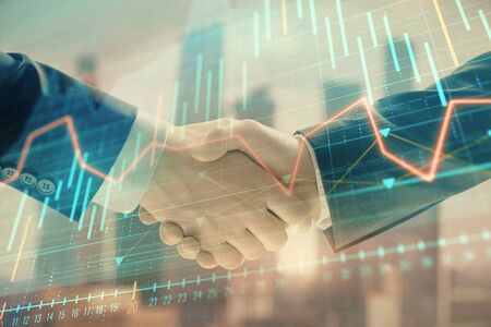 Double exposure of financial graph on cityscape background with two businessman handshake. Concept of stock market dealの写真素材