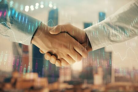 Double exposure of financial graph on cityscape background with two businessman handshake. Concept of stock market dealの写真素材