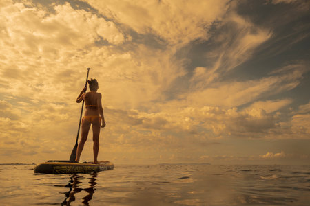 woman paddling on a surfboard under a dramatic sky, Estalella, coast of Llucmajor, Majorca, Balearic...