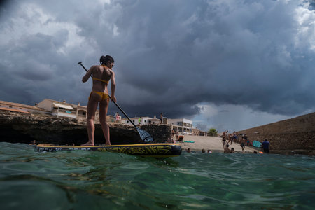 woman paddling on a surfboard under a dramatic sky, Estalella, coast of Llucmajor, Majorca, Balearic Islands, Spainの写真素材