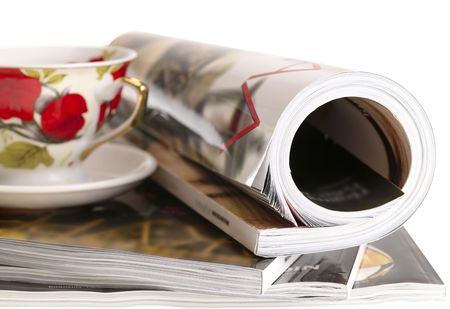 Woman's rolled glossy magazine in stack with tea cup.の写真素材