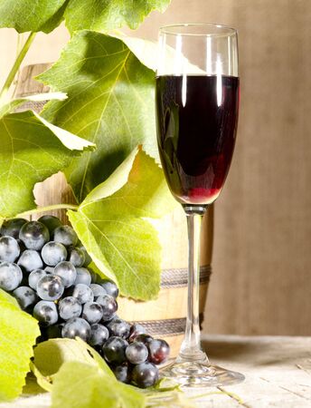 Old red wine in glass with vine and grape under the sun lightの写真素材