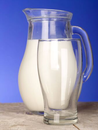Milk jug close to glass on the table with blue backgroundの写真素材