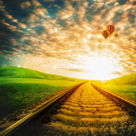 Railroad through the green valley, under blue skies with air balloonsの写真素材